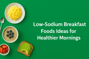 A colorful flat lay of healthy low-sodium breakfast foods such as scrambled eggs, blueberry oatmeal, avocado toast, and strawberries against a green background with the caption "Low-Sodium Breakfast Foods Ideas for Healthier Mornings." Ideal image for an article on healthy, low-sodium breakfast ideas to promote heart health and healthy mornings.